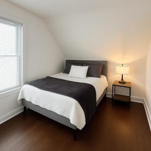 a bedroom with a bed and a lamp on a wooden floor at Hidden Gem Steps From River, Restos, Cafés, Parks in Windsor
