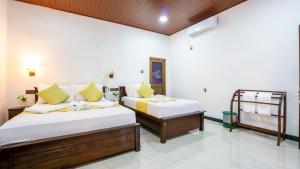 two beds in a room with white walls and yellow pillows at Tranquil Guest in Sigiriya