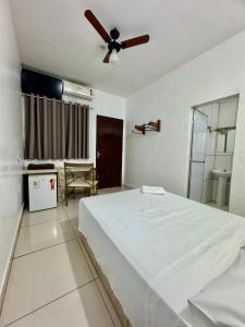 a bedroom with a white bed and a ceiling fan at Hotel Caiçara Matão in Matão
