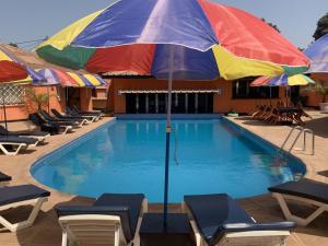 a pool with chairs and a colorful umbrella at Avalon Garden Lodge in Banjul +9 photos