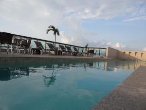 a swimming pool with chairs and a building and a palm tree at Residence Flat Prime Itaboraí in Itaboraí