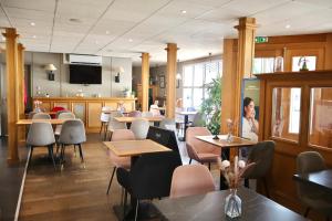 a restaurant with tables and chairs and a woman at Brit Hotel Essentiel Reims Taissy in Reims