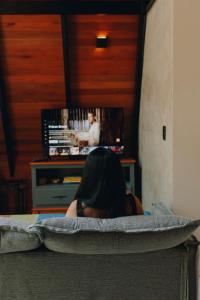 a woman sitting on a bed watching a tv at Chalé Elemental in Morretes