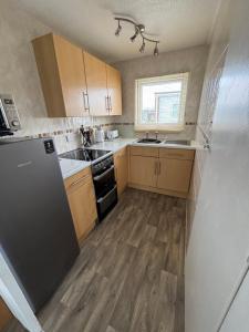 a kitchen with wooden cabinets and a black refrigerator at 192, Two bed newly refurbished chalet on Sund0wner Holiday Park - Sleeps 5, pet friendly - Includes electricity, bed linen and towels - Entertainment options close by in Hemsby