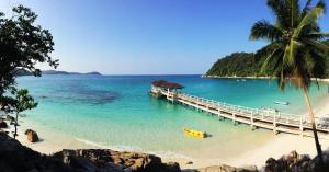 a beach with a pier and a yellow boat on the water at Perhentian Island Resort in Perhentian Islands