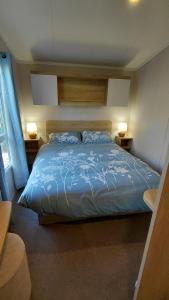 a bedroom with a bed with blue sheets and two lamps at Driftwood at Freshwater Beach Holiday Park in Burton Bradstock