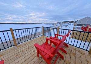 two red chairs sitting on a deck next to the water at Saltwater Steeple in Port Saunders