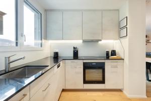 a kitchen with white cabinets and a sink at Spacious & Modern Apt - Balcony & Parking in Spiez