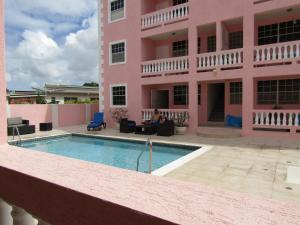 a person sitting in front of a pink building with a pool at Sandy Cove in Christ Church