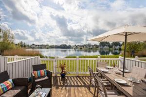 a wooden deck with a table with an umbrella and a lake at Lakefront Lodge w SUP & Fishing Access Cotswolds in Gloucestershire