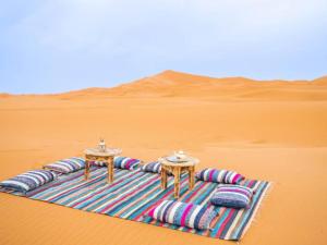 a blanket in the desert with two tables and pillows at Dream Land Camp in Merzouga