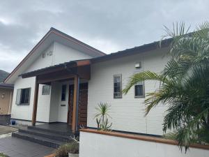 a white house with a porch and a palm tree at SerenityBlueAmami in Tatsugo