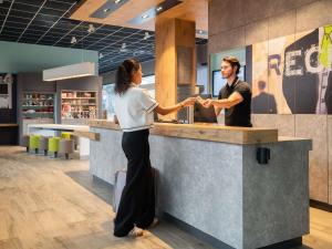 a man and a woman shaking hands at a counter at ibis budget Geneve Palexpo Aeroport in Geneva