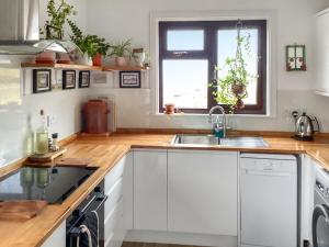 a kitchen with white cabinets and a sink and a window at At Last in Rhiconich