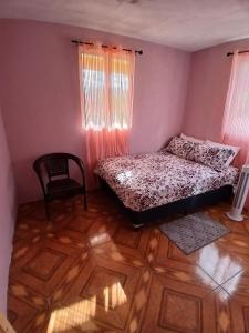 a bedroom with a bed and a chair and wooden floors at Valley View Inn in Roseau