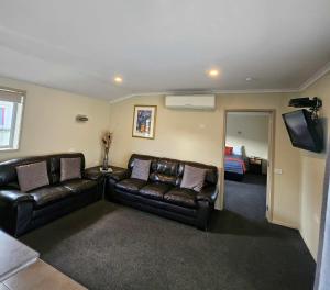 a living room with two leather couches and a bed at Scenicland Motels in Greymouth