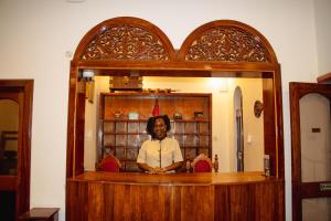 a woman standing behind a counter in a mirror at Shangani Hotel in Zanzibar City