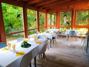 a dining room with white tables and chairs and windows at Diana Panzió in Mátrafüred