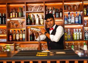 a man standing behind a bar with a bottle of alcohol at Ramadia Ran Mal Holiday Resort in Moratuwa