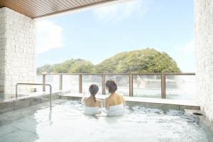 two women sitting in a bath tub with a view at Ooedo Onsen Monogatari Premium Toba Saichoraku in Toba