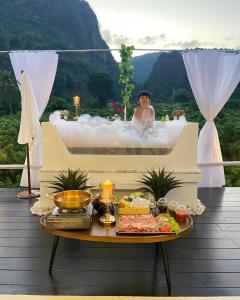 una donna in una vasca da bagno con un tavolo imbandito di cibo di บ้านสวนจมูกโต a Ban Pha Mi