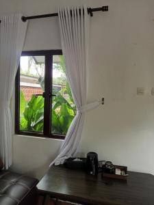 a window with white curtains and a wooden table at Ratu Roso Resort in Malang