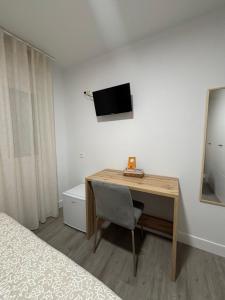 a bedroom with a desk and a television on the wall at Hostal Los Rosales in Tejeda de Tiétar