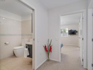a bathroom with a toilet and a vase with red flowers at Soleil Studio - Whangamata Self-contained Unit in Whangamata +12 photos