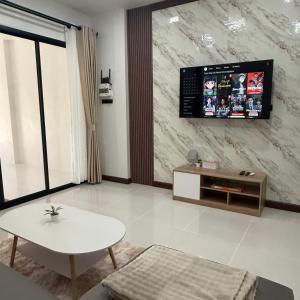 a living room with a table and a tv on a wall at O Pha Suk House in Hat Yai