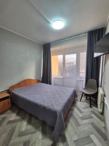 a bedroom with a bed and a chair and a window at Альтаир in Almaty