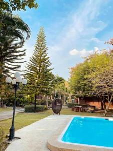 a swimming pool in a park with a tree and a lamp at Mireya Resort Khaoyai in Ban Khanong Phra Nua