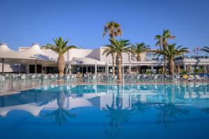 a large swimming pool with palm trees and a building at Lyttos Beach in Hersonissos