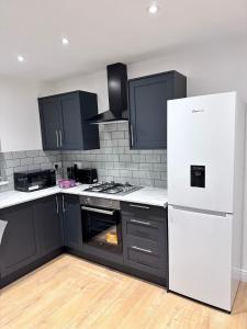 a kitchen with black cabinets and a white refrigerator at Modern 4 Bedroom House Sleeps 10 Free Parking Liverpool in Litherland