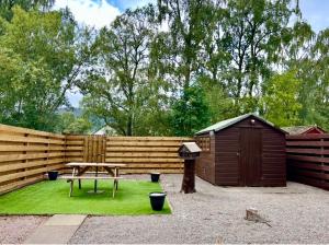 a wooden fence with a picnic table and a shed at Rendezvous , Aviemore in Aviemore