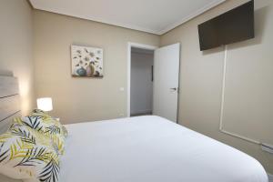 a white bedroom with a bed and a flat screen tv at AP Home Carretería in Cuenca