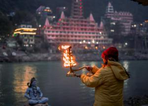 a woman holding a lit candle in front of a building at Hotel Ishan - A Ganges Riverside Retreat by Salvus in Rishīkesh