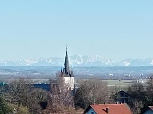 a church with a spire with mountains in the background at Ferienwohnung Soherr in Erolzheim