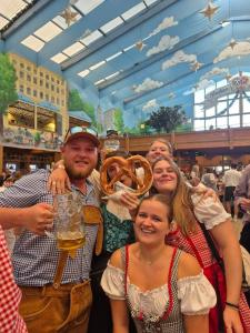 a group of people posing for a picture with a pretzel at Beer Base-Camp 'BASIC PACKAGE' Oktoberfest Camping, with free welcome beer and traditional lederhosen-dirndl shop in Munich