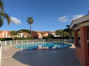 a swimming pool with a fence and palm trees at Mazet avec piscine collective in Le Lavandou