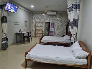 two beds in a room with a table and a tv at Abi Hotel & Rastaurant in Jaffna