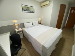 a bedroom with a white bed and a black chair at Samba Rio Bonito in Rio Bonito