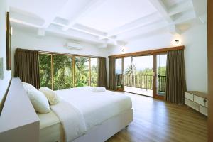 a white bedroom with a large bed and a balcony at Segara Hill Villa in Senggigi