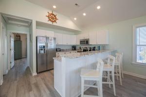 a kitchen with white cabinets and a bar with stools at Savannah - Nags Head MP 16, Oceanfront, Direct Beach Access, Pool, Hot Tub, Pool Table in Nags Head