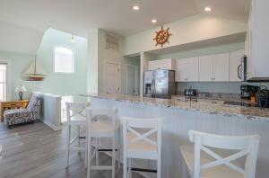 a kitchen with a bar with white cabinets and white stools at Savannah - Nags Head MP 16, Oceanfront, Direct Beach Access, Pool, Hot Tub, Pool Table in Nags Head +71 photos