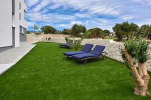 a yard with two blue chairs on a green lawn at Pool Apartments & Rooms Mare in Novalja