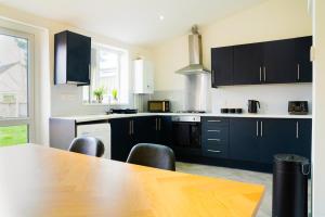 a kitchen with black cabinets and a wooden table at 4 BD Sleeps 7 Parking WiFi in Coventry +36 photos