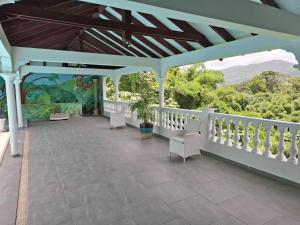 a covered porch with white chairs and a view of the mountains at Le Chalet d'Ajoupa in LʼAjoupa-Bouillon