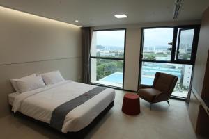 a bedroom with a bed and a chair and windows at Hotel Skypark DaejeonⅠ in Daejeon