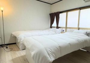 two beds in a room with white sheets and a window at Nishijin Stay One in Fukuoka