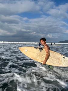 a man standing in the water holding a surfboard at Casa bohio surf in Jacó